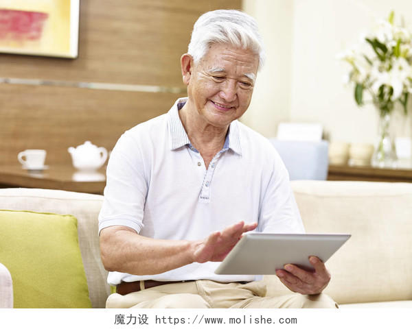 一位老年人微笑着坐在沙发上使用平板电脑放松微笑的老人